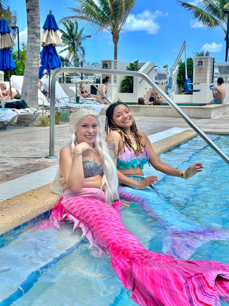 Two AquaMermaid performers of different backgrounds at a resort pool