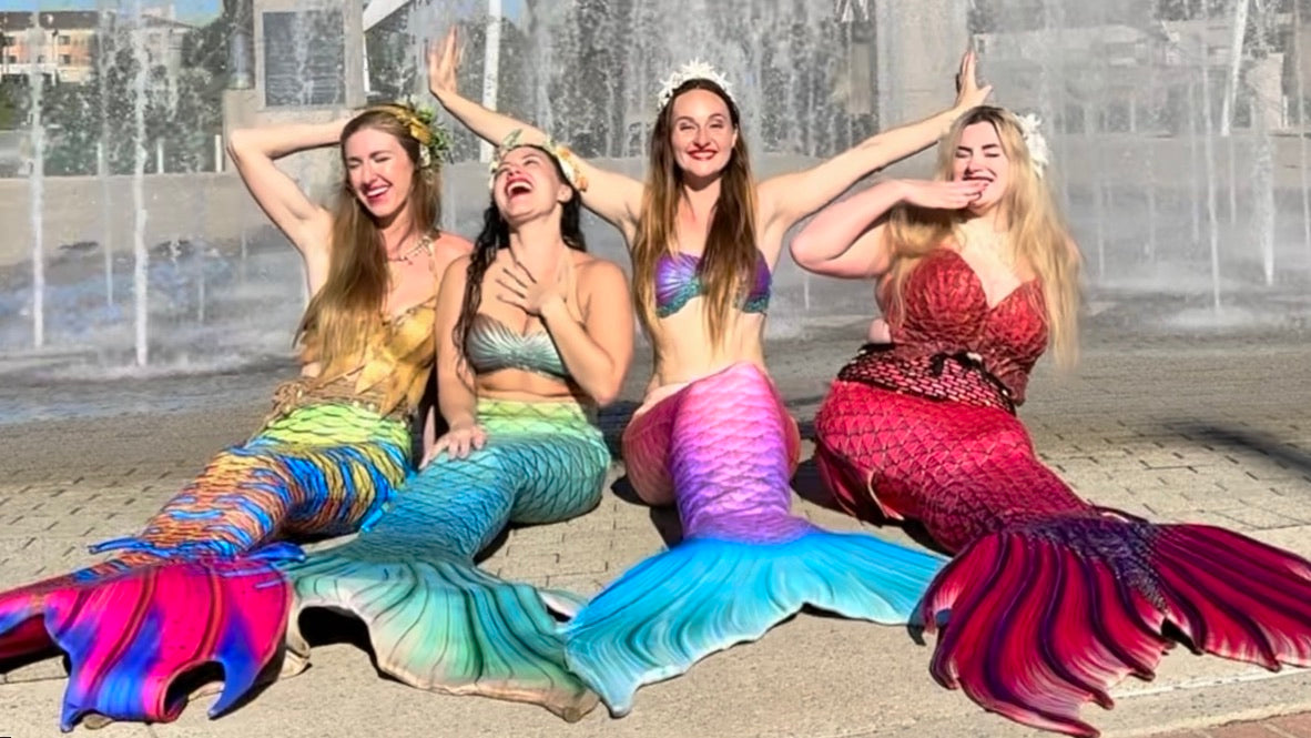 Four AquaMermaid performers in colorful tails laughing together